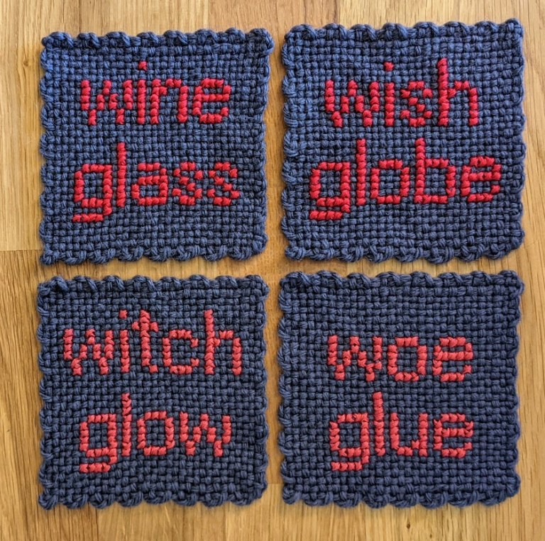 four purple coasters, sewn in hot pink with the following words: wine glass, wish globe, witch glow, woe glue